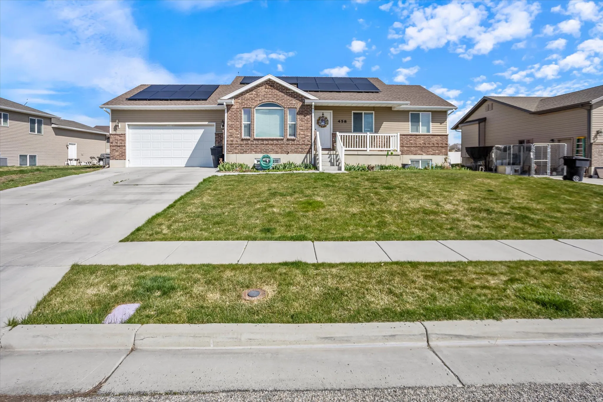 Ranch-style home with covered porch, roof mounted solar panels, brick siding, a front yard, and driveway
