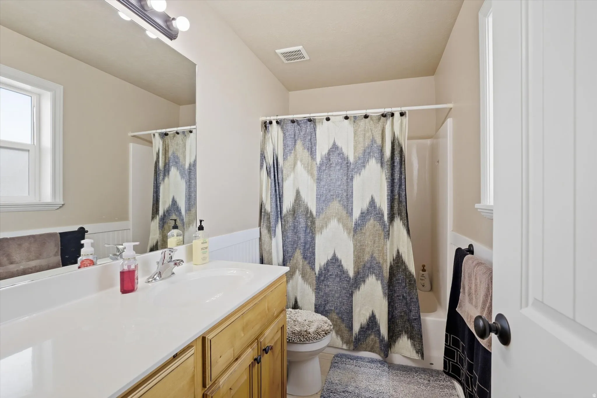 Bathroom with a wainscoted wall, vanity, and shower / bath combo with shower curtain