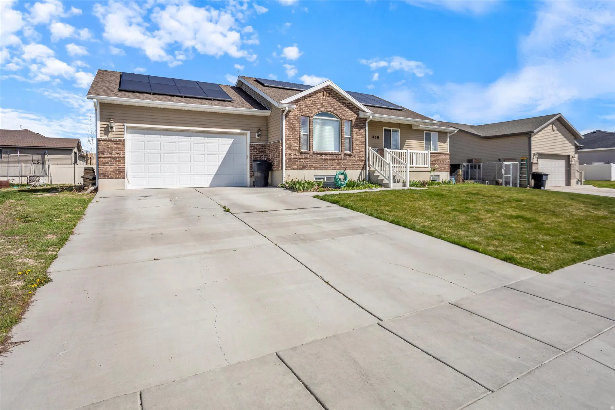 Single story home featuring covered porch, driveway, a garage, brick siding, and roof mounted solar panels