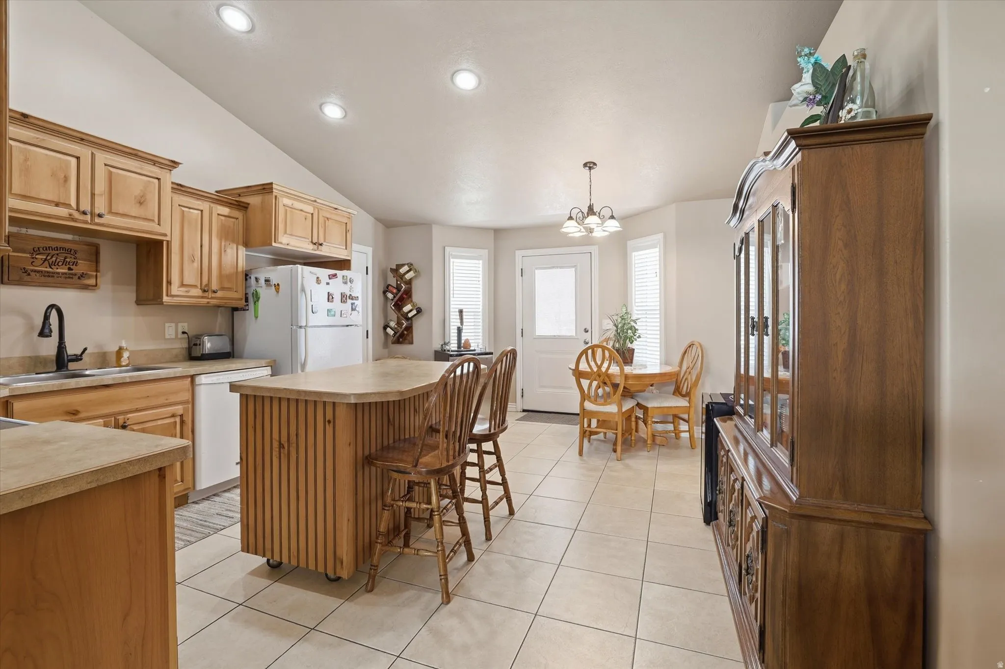 Kitchen featuring a kitchen island, light tile patterned floors, light countertops, lofted ceiling, and white appliances