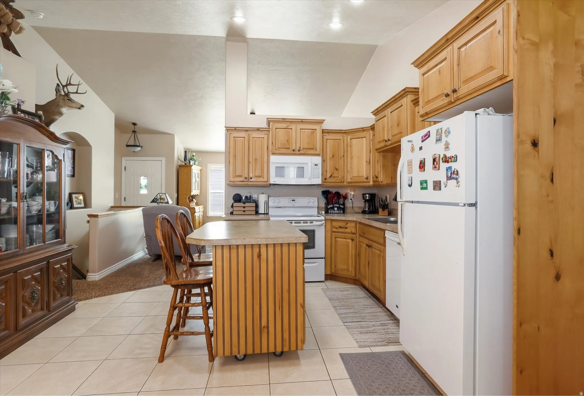 Kitchen with white appliances, lofted ceiling, a kitchen island, light countertops, and a breakfast bar