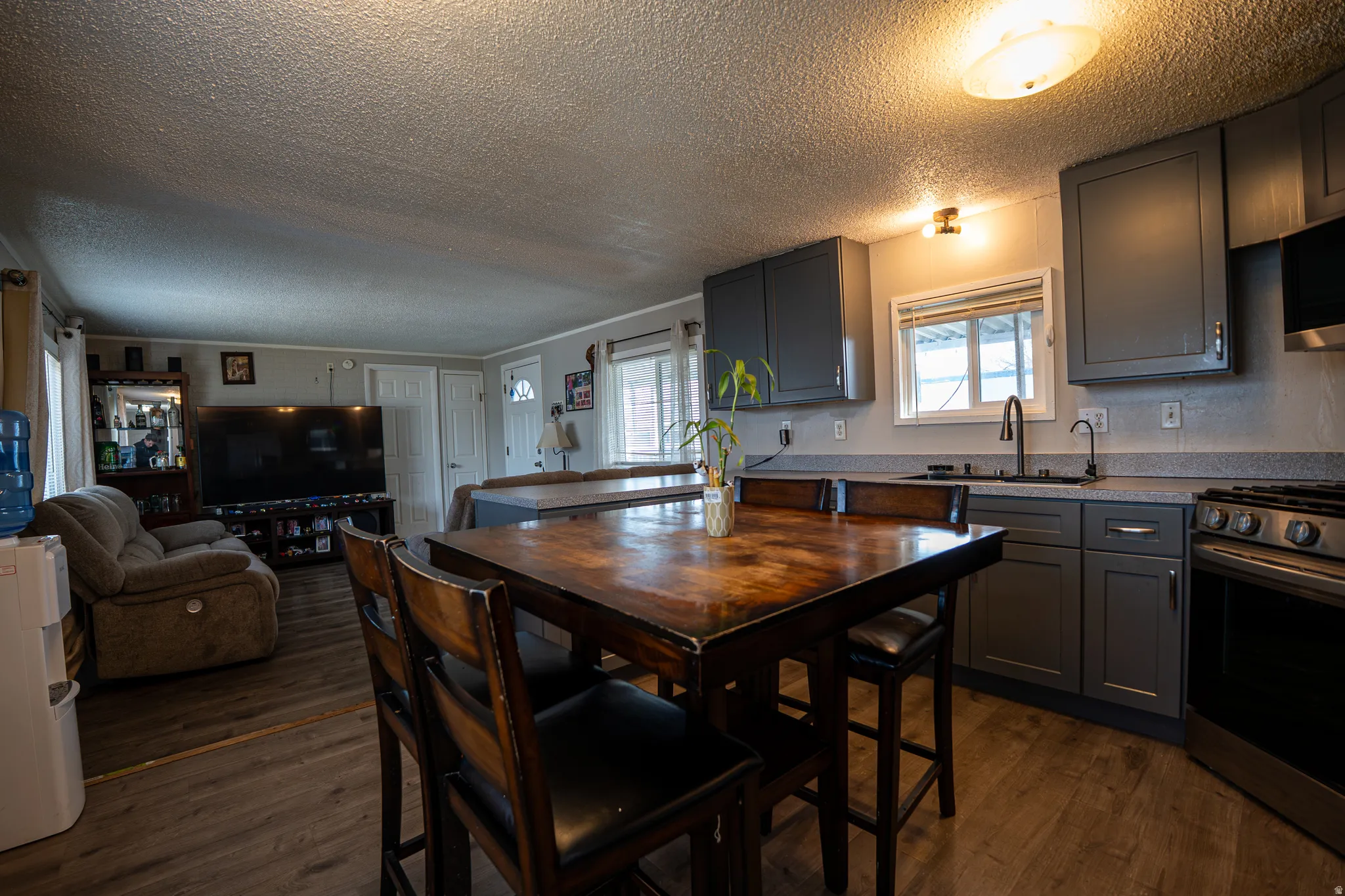 Kitchen featuring stainless steel appliances, a textured ceiling, gray cabinets, dark wood-style flooring, and open floor plan