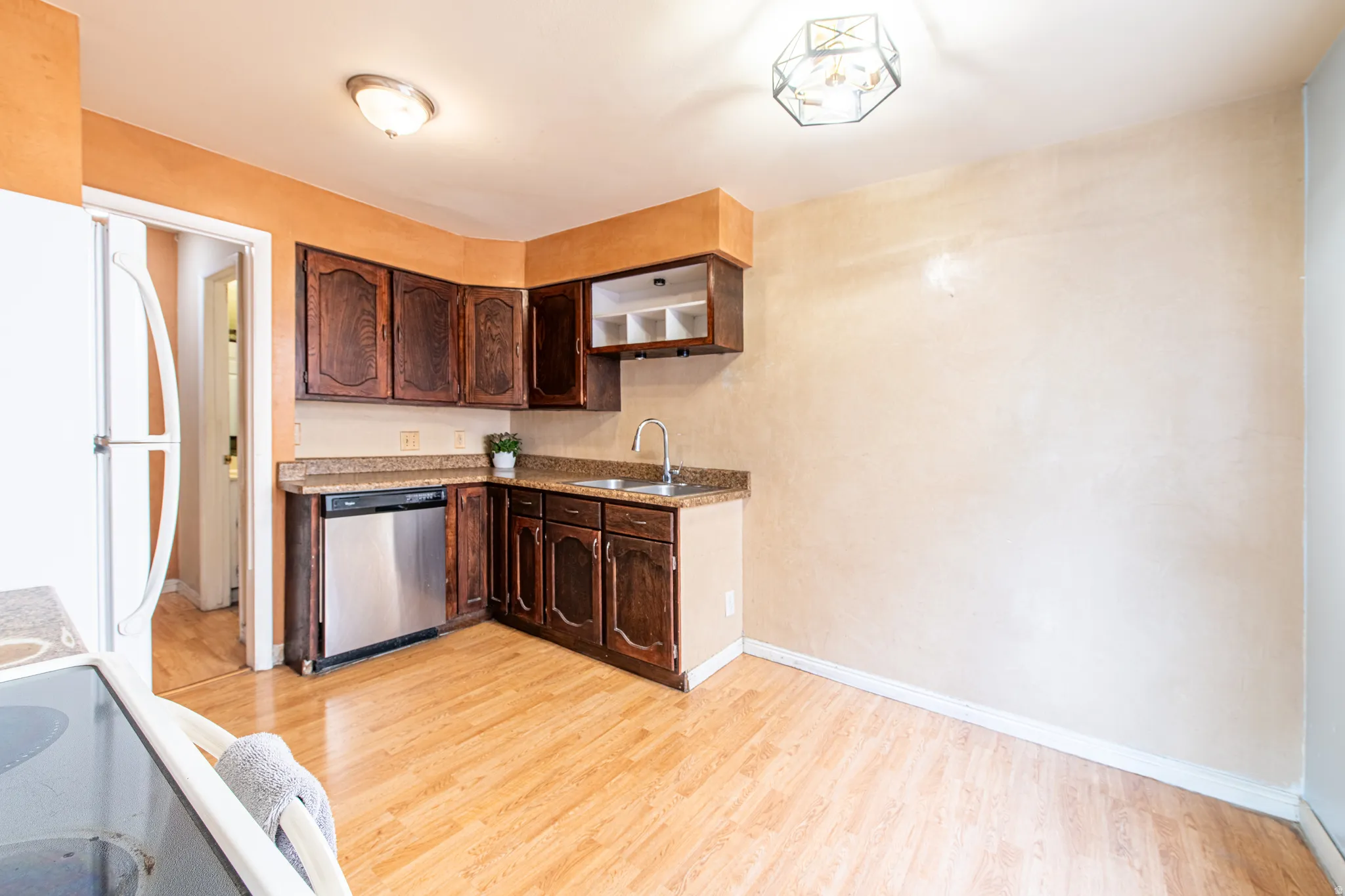 Kitchen with dark wood finish cabinets, freestanding refrigerator, light wood finished floors, stainless steel dishwasher, and range with electric stovetop