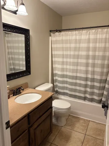 Bathroom with vanity, a textured ceiling, shower / bath combination with curtain, and light tile patterned floors