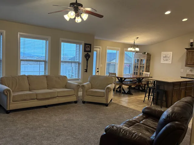 Living area with a ceiling fan, hanging lights, light carpet, and vaulted ceiling