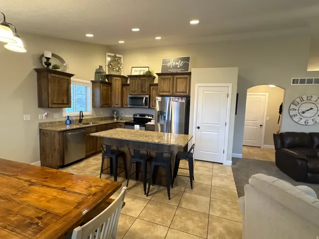 Kitchen featuring arched walkways, dark wood finish cabinetry, light stone countertops, a kitchen breakfast bar, and stainless steel appliances