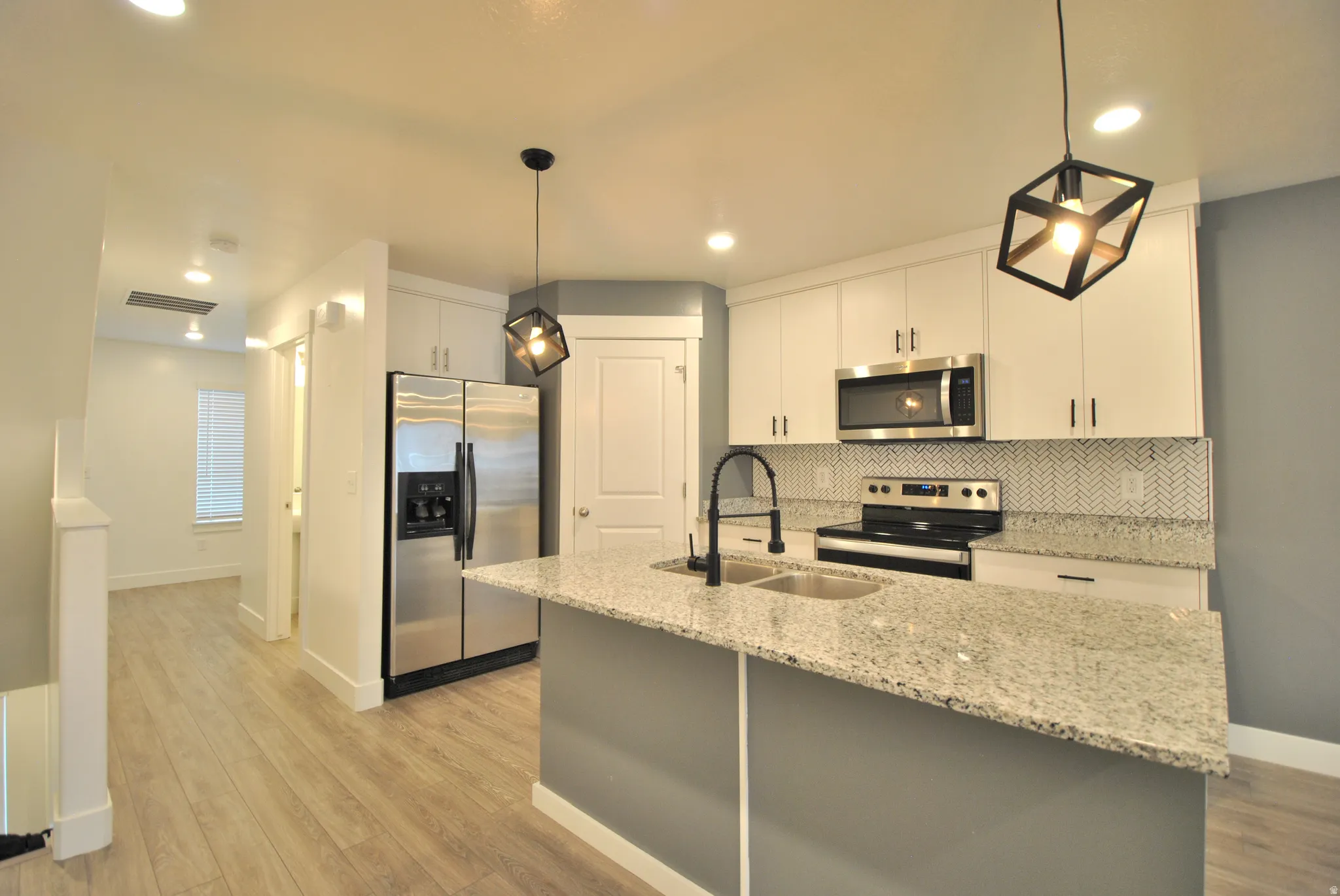 Kitchen featuring stainless steel appliances, pendant lighting, light stone counters, and light wood finished floors