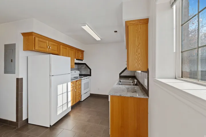 Kitchen with light stone counters, white appliances, electric panel, tasteful backsplash, and wood finish cabinetry