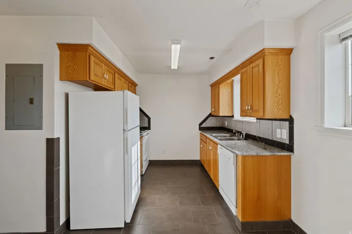 Kitchen with electric panel, backsplash, light stone counters, white appliances, and wood finish cabinets