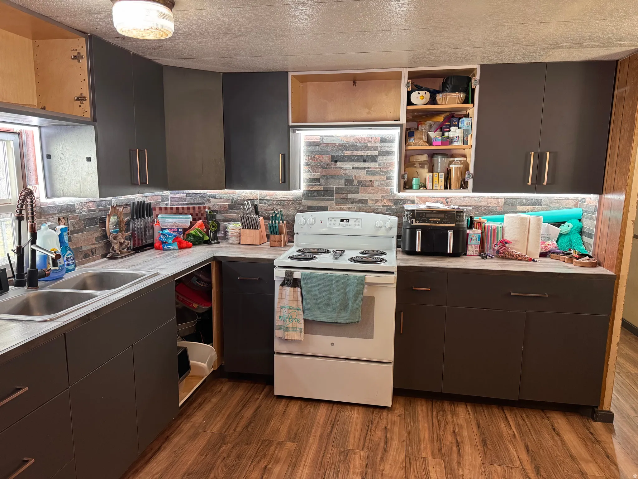 Kitchen featuring white range with electric stovetop, light countertops, open shelves, dark wood-style floors, and a textured ceiling