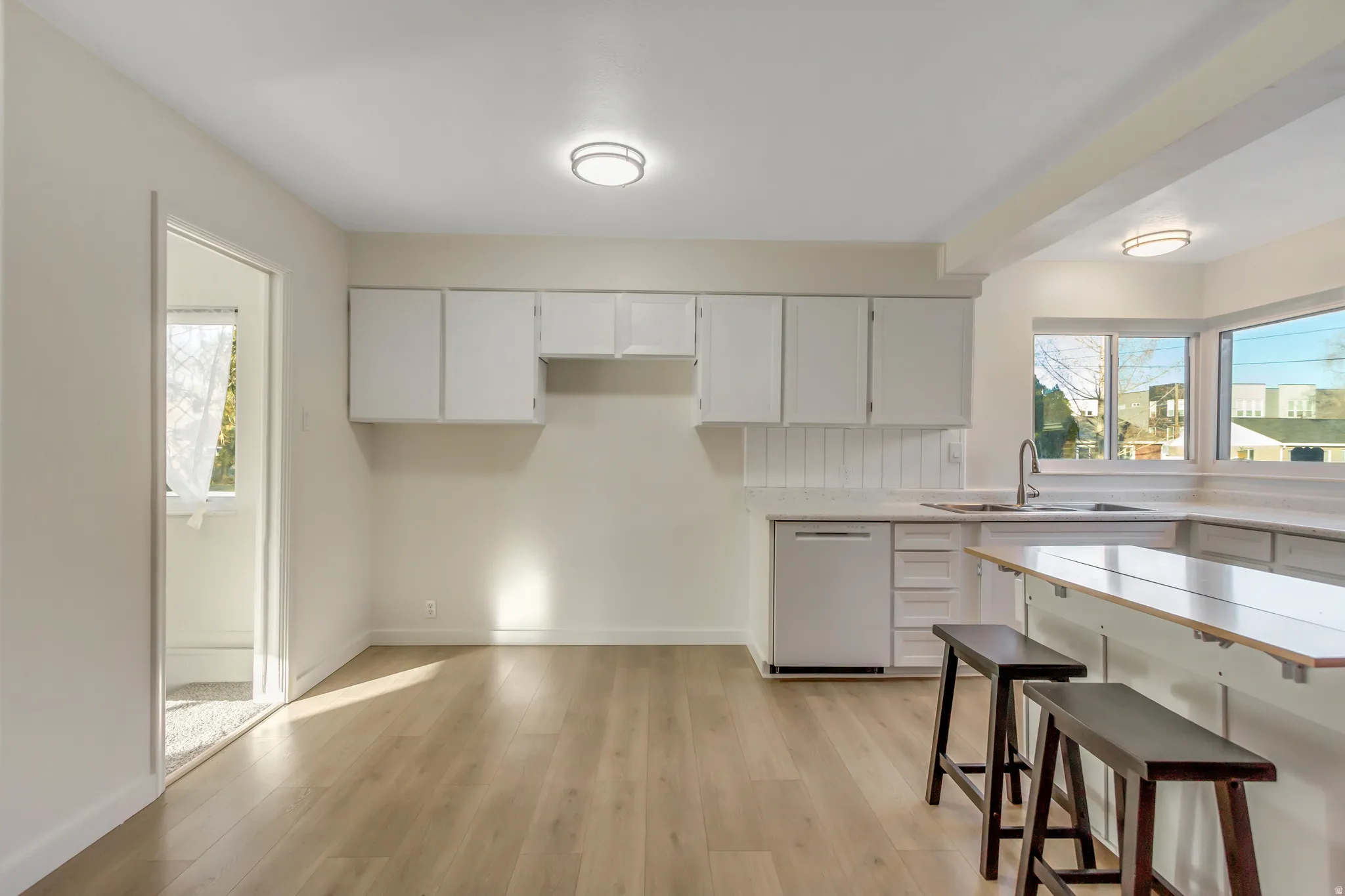 Kitchen featuring light wood finished floors, white cabinets, dishwashing machine, a kitchen bar, and healthy amount of natural light