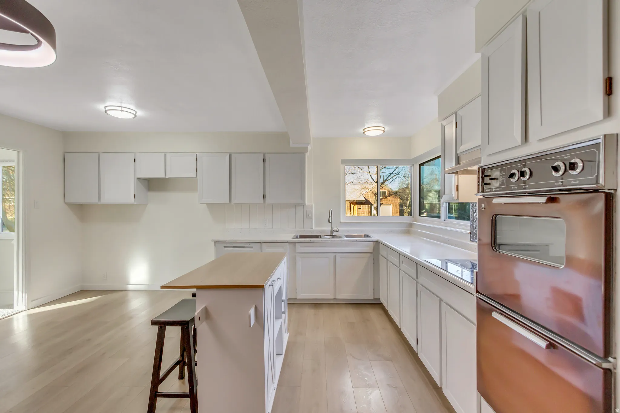 Kitchen featuring beam ceiling, a breakfast bar, light wood-style flooring, a warming drawer, and white cabinets