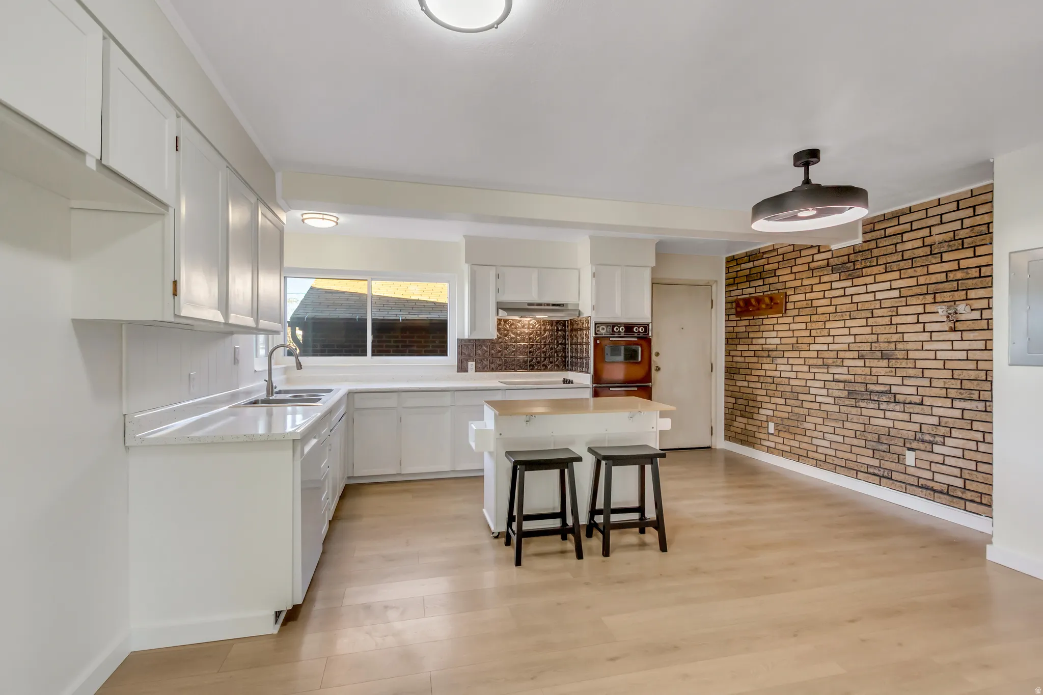 Kitchen featuring white cabinets, a breakfast bar area, a center island, light wood finished floors, and brick wall