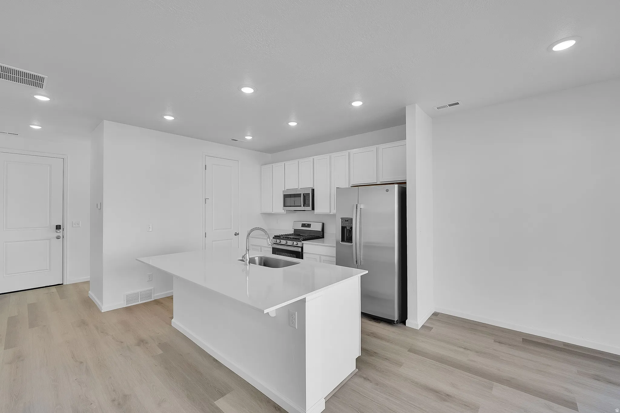 Kitchen featuring stainless steel appliances, white cabinets, an island with sink, recessed lighting, and light wood-style flooring