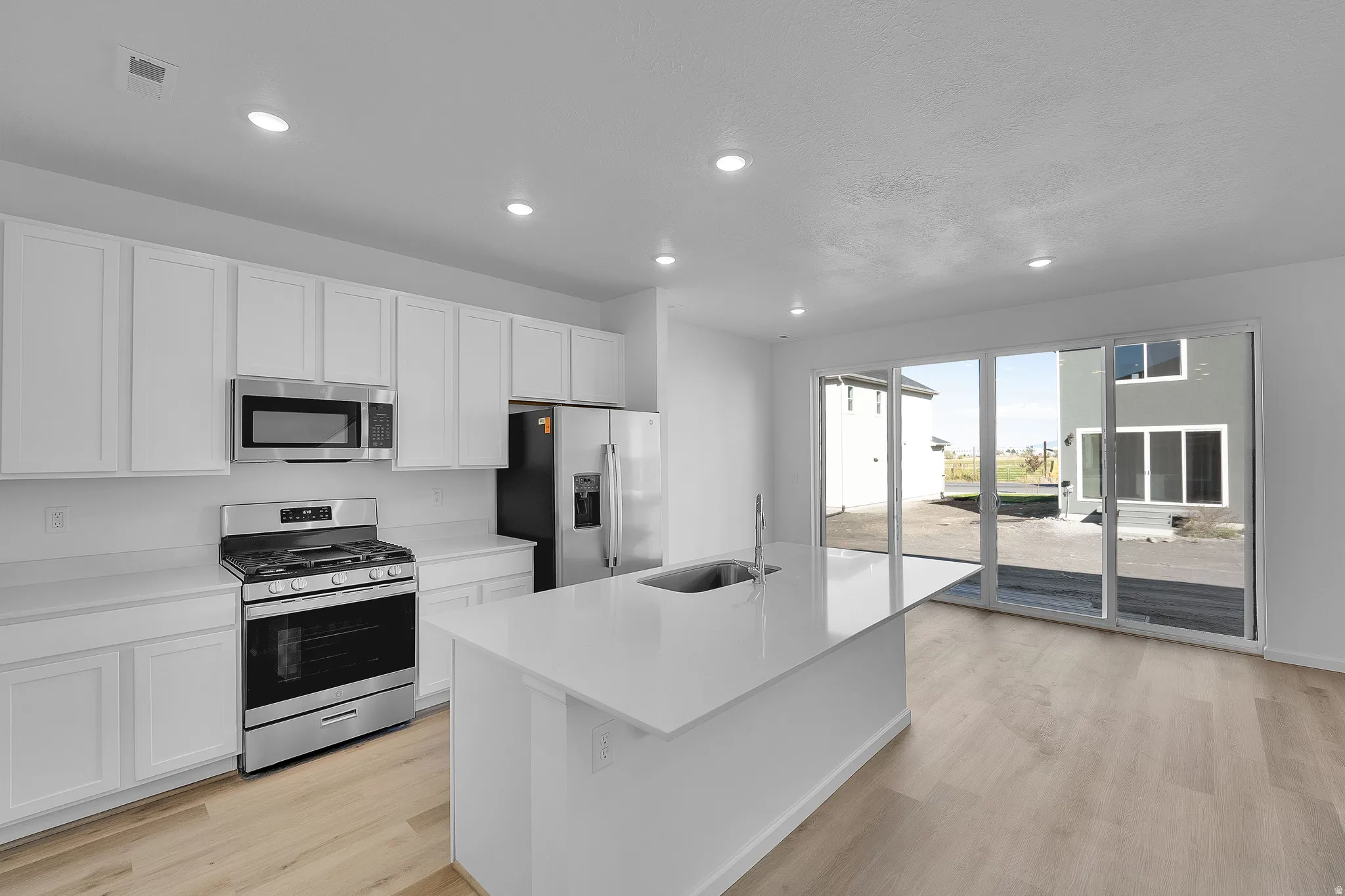 Kitchen featuring stainless steel appliances, white cabinets, light wood-style floors, a center island with sink, and recessed lighting