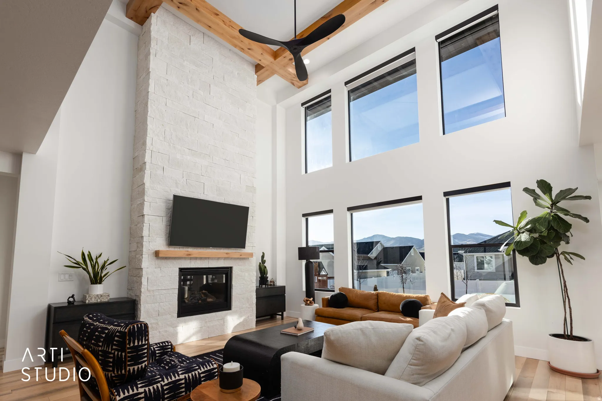 Living room with a fireplace, light wood-style floors, a towering ceiling, beam ceiling, and a ceiling fan