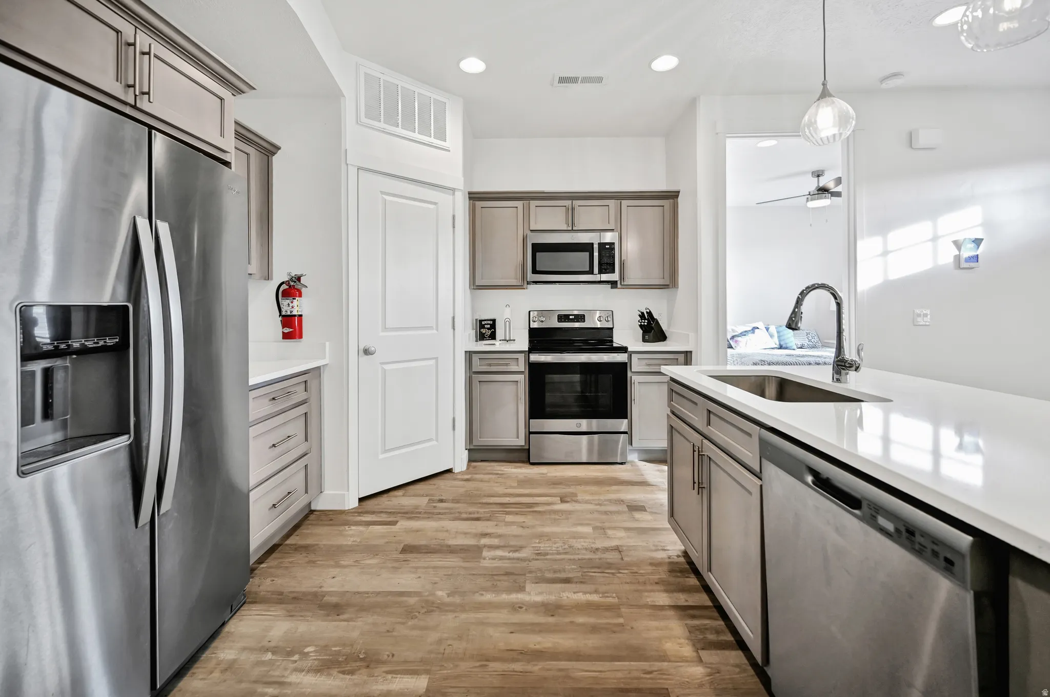 Kitchen featuring stainless steel appliances, decorative light fixtures, light wood-style flooring, light stone countertops, and ceiling fan