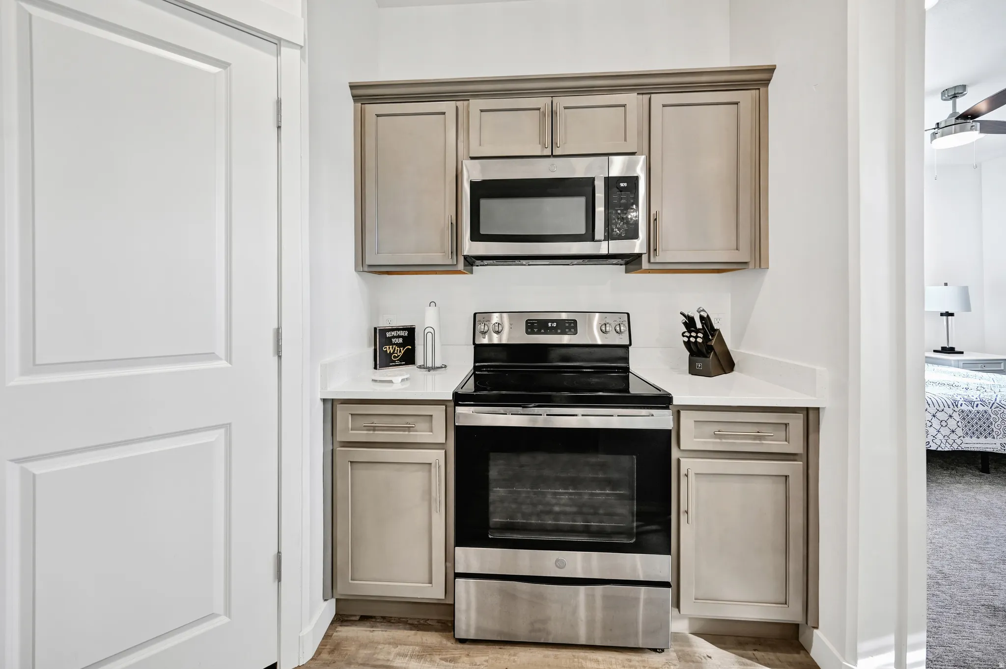 Kitchen featuring stainless steel appliances, ceiling fan, light wood-style flooring, and light stone counters