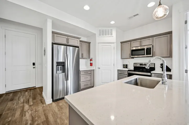 Kitchen featuring light stone counters, stainless steel appliances, hanging light fixtures, and light wood-type flooring