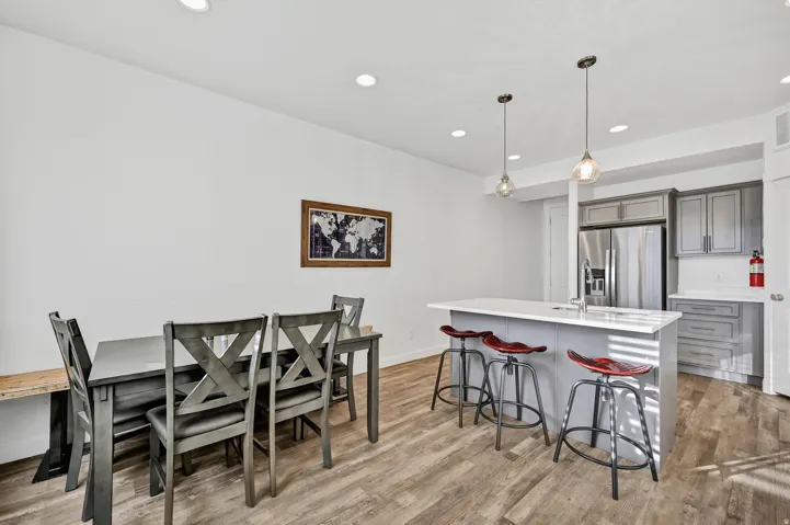 Kitchen featuring decorative light fixtures, gray cabinetry, an island with sink, a kitchen bar, and stainless steel fridge