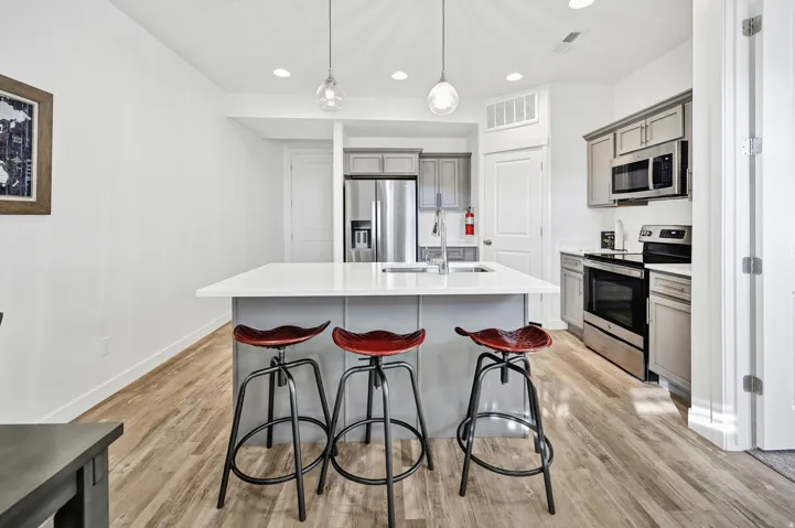 Kitchen featuring stainless steel appliances, gray cabinets, hanging light fixtures, a breakfast bar, and light wood-type flooring