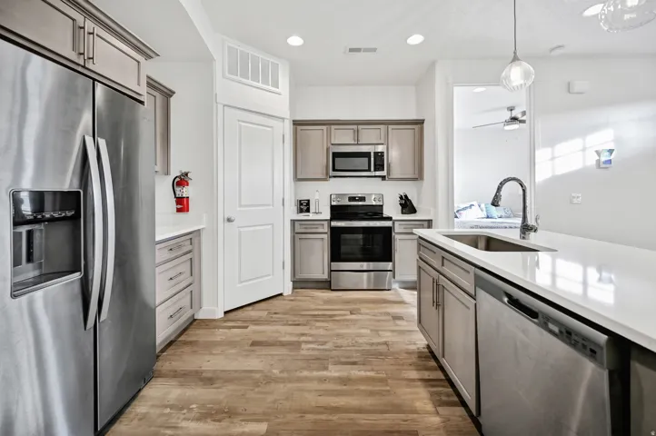 Kitchen featuring stainless steel appliances, decorative light fixtures, light wood-style flooring, light stone countertops, and ceiling fan
