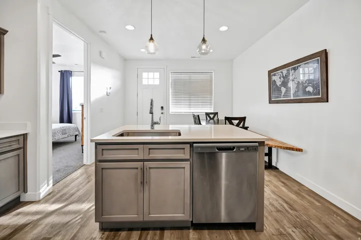 Kitchen with dishwasher, hanging light fixtures, a center island with sink, light wood-type flooring, and light stone countertops