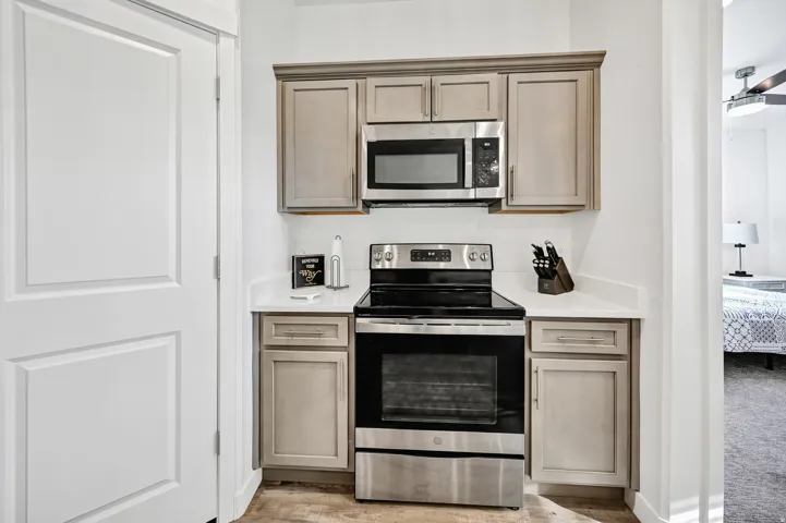 Kitchen featuring stainless steel appliances, ceiling fan, light wood-style flooring, and light stone counters