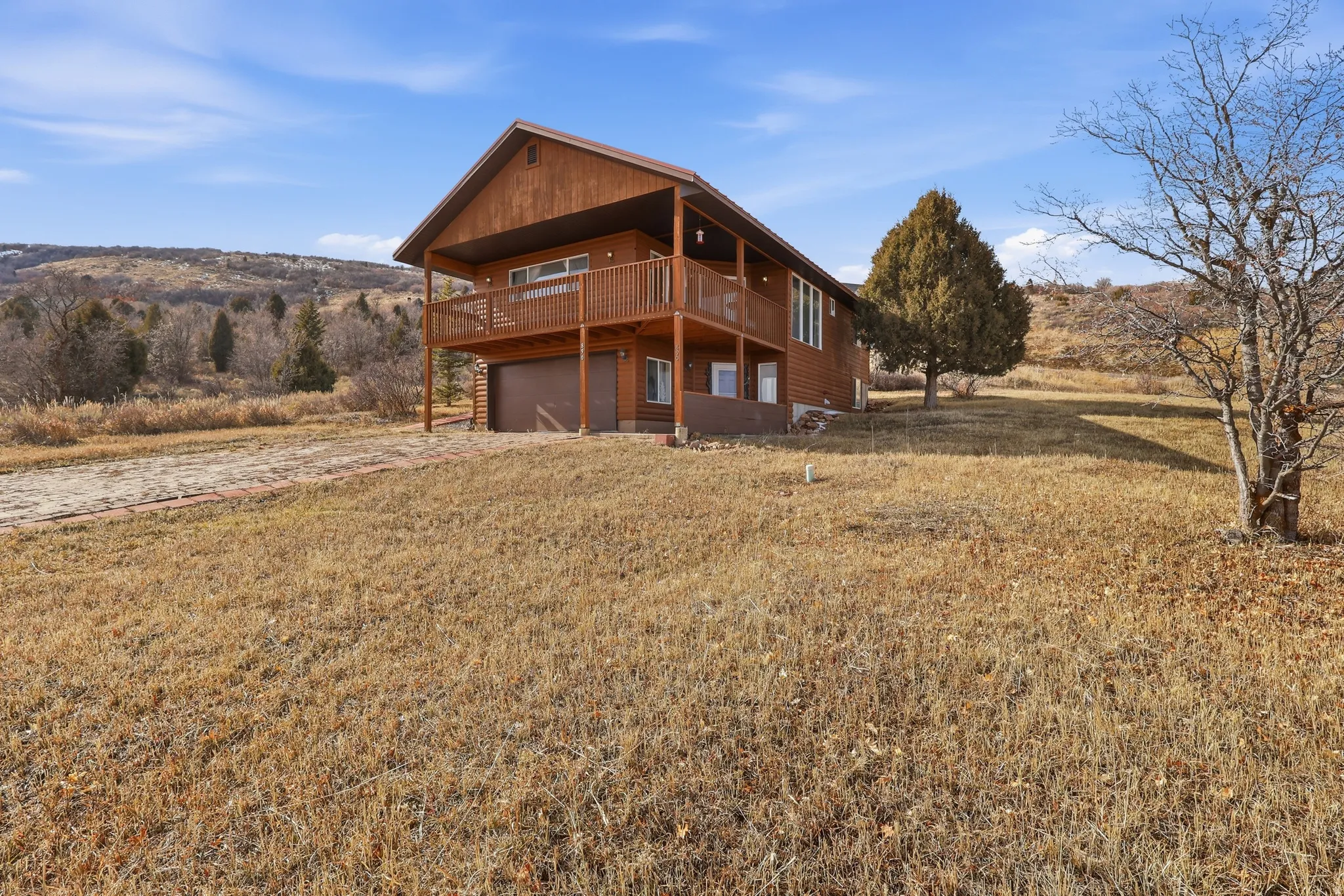 Rear view of property with a lawn, driveway, a garage, and a deck with mountain view