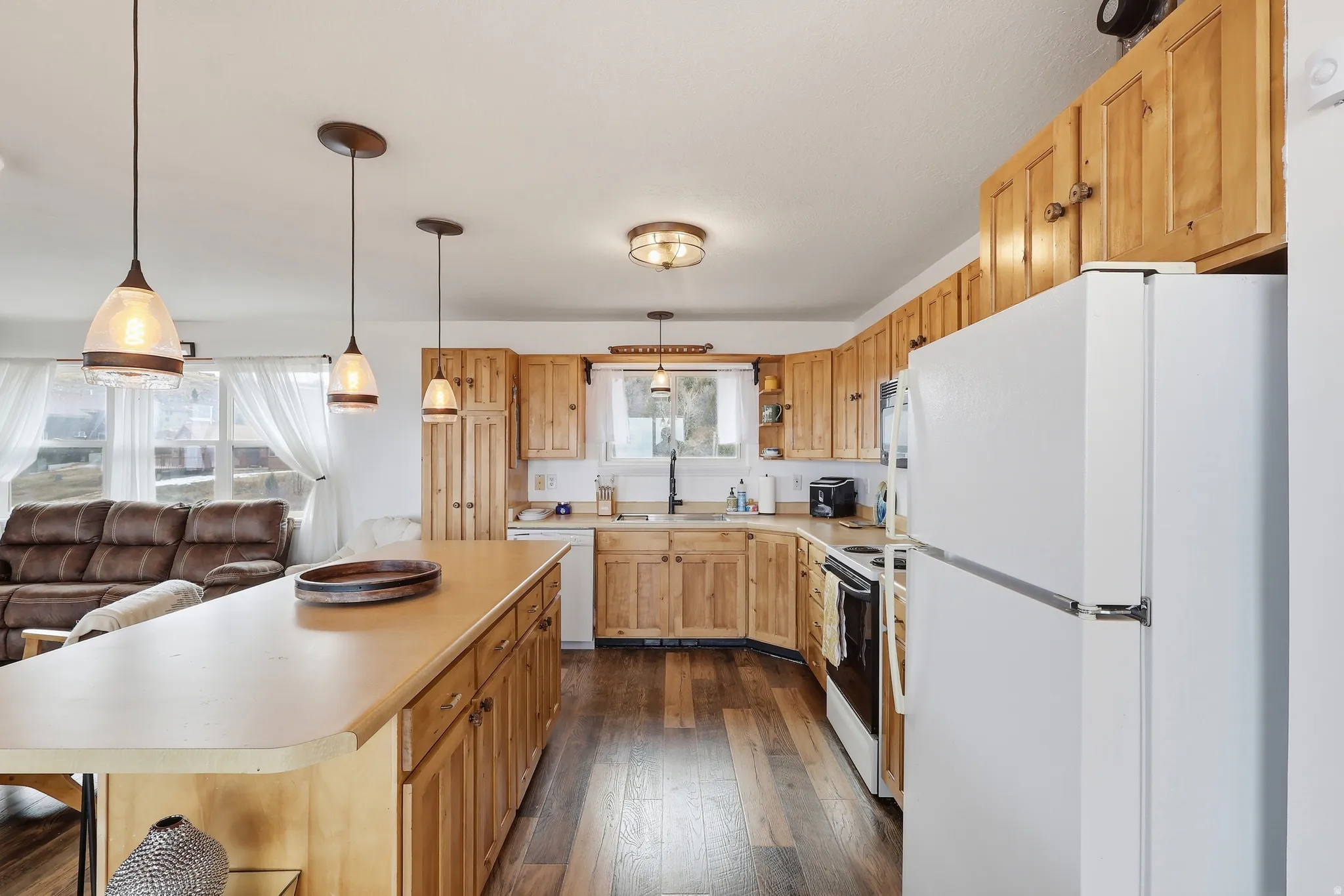 Kitchen featuring white appliances, light countertops, a breakfast bar area, decorative light fixtures, and dark wood finished floors