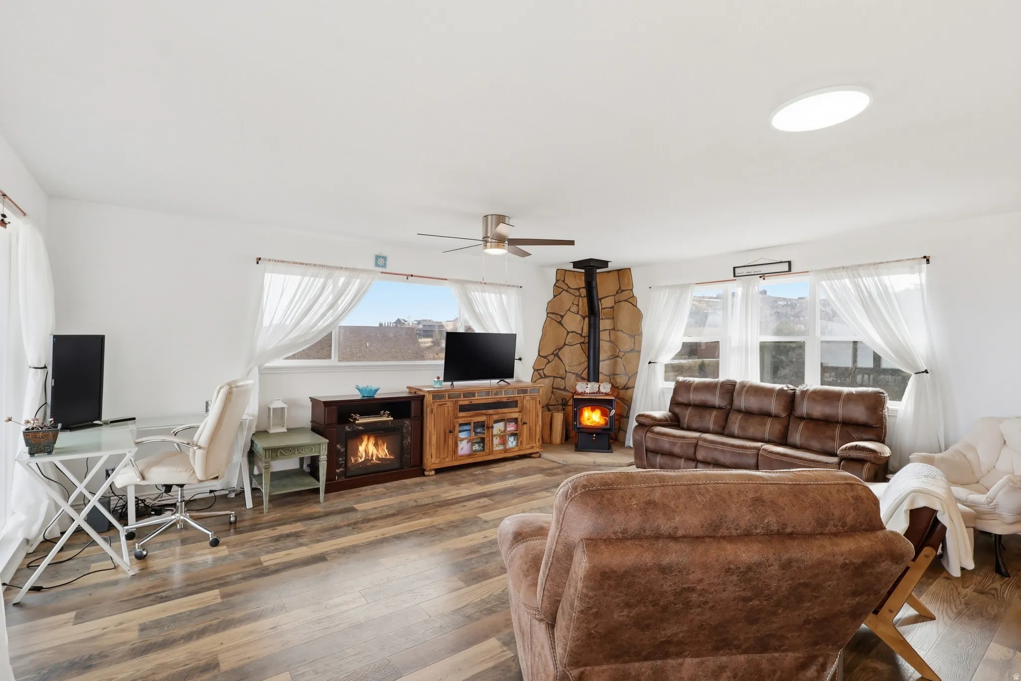 Living room with hardwood / wood-style floors, a ceiling fan, a desk, and a wood stove