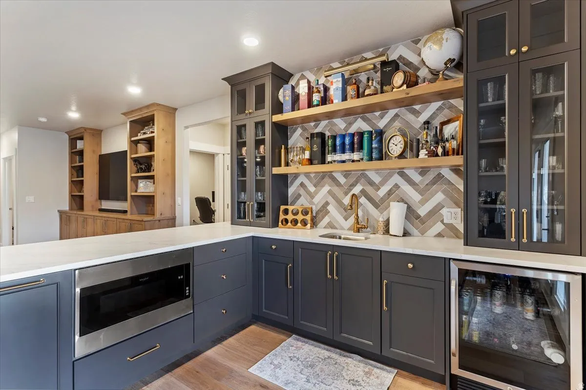Indoor wet bar with wine cooler, decorative backsplash, stainless steel microwave, light stone countertops, and open shelves