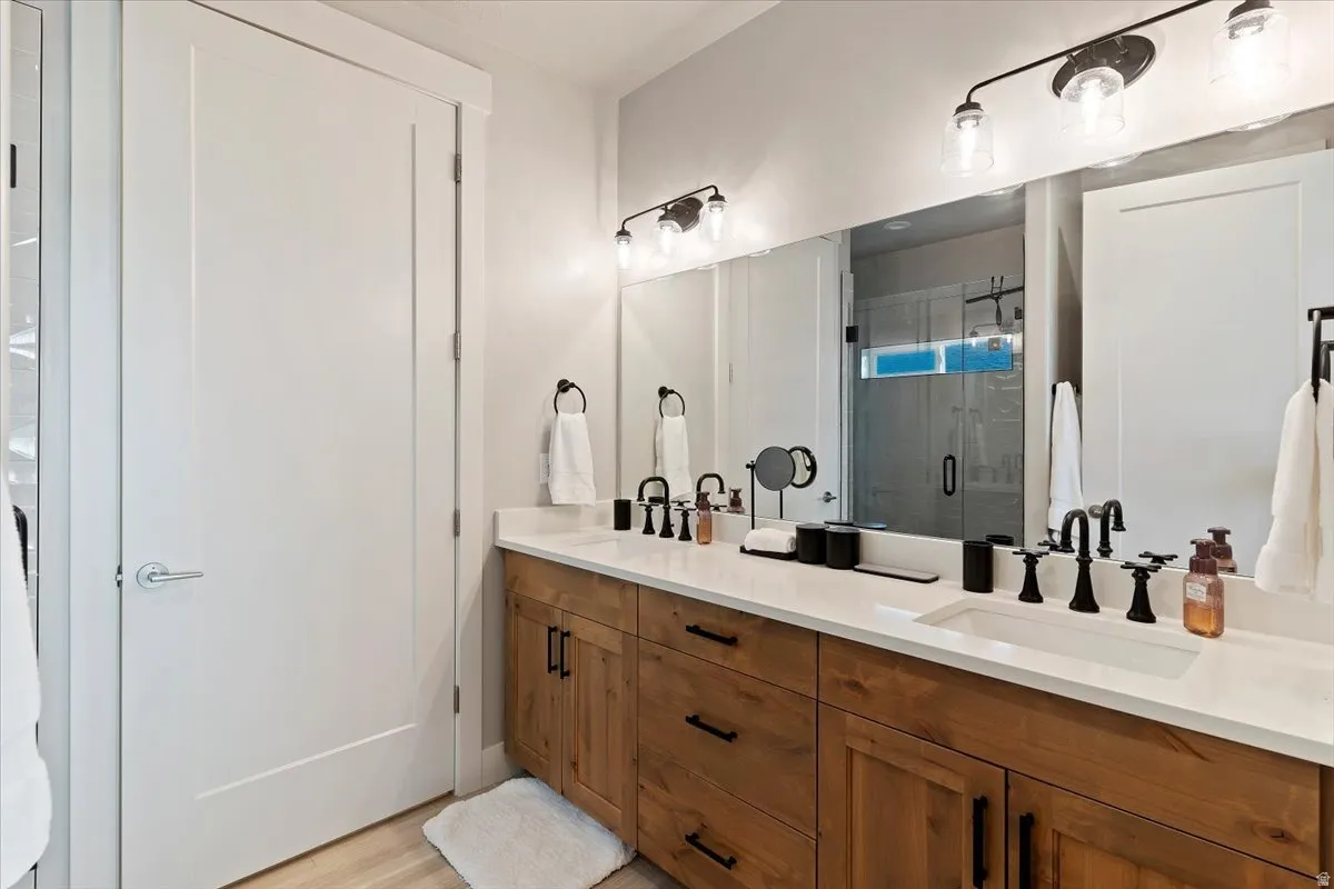 Full bath with double vanity, a stall shower, and light wood-type flooring