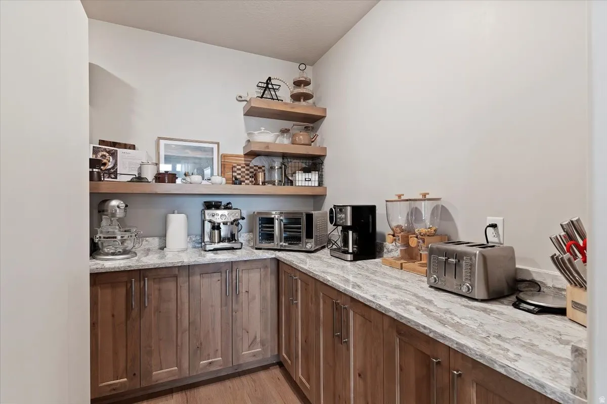 Bar area with open shelves, light stone counters, light wood-style floors, and wood finish cabinets