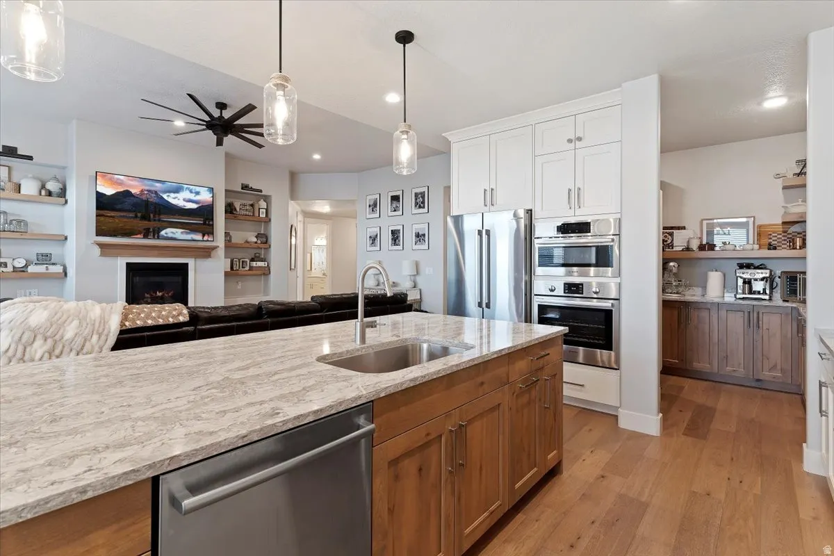 Kitchen featuring pendant lighting, open floor plan, stainless steel appliances, dual tone cabinetry, and a lit fireplace