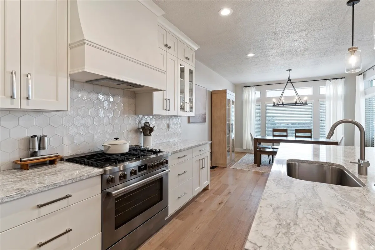 Kitchen featuring stainless steel gas range oven, light stone counters, white cabinets, and a textured ceiling