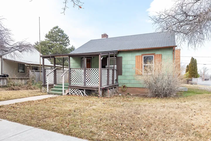 View of front facade with a front yard, a wooden deck, roof with shingles, and a chimney