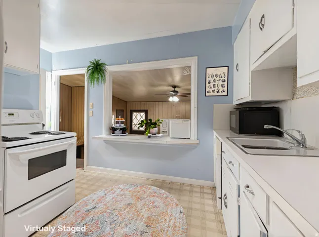 Kitchen with light flooring, white cabinets, electric range, light countertops, and black microwave
