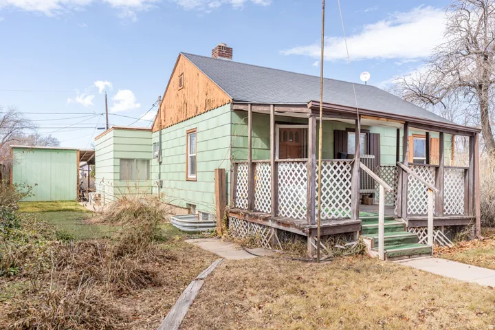View of front of home featuring a deck, roof with shingles, a front lawn, a chimney, and a storage shed
