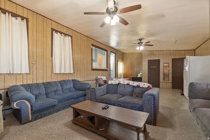 Carpeted living room with ceiling fan and wood walls