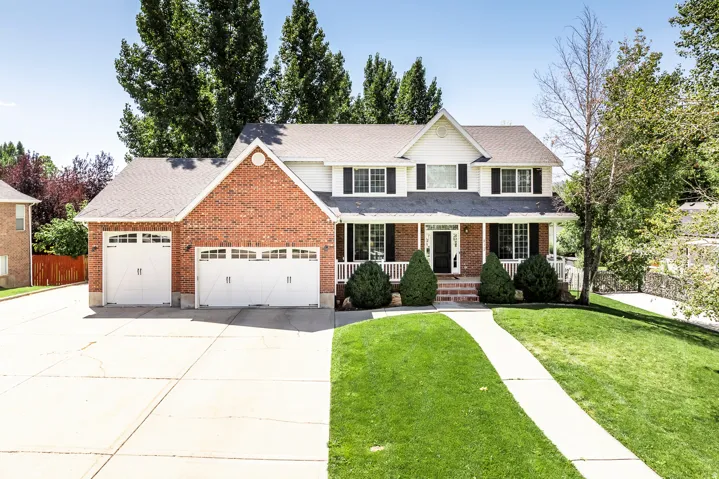Traditional-style home with covered porch, a garage, driveway, brick siding, and roof with shingles