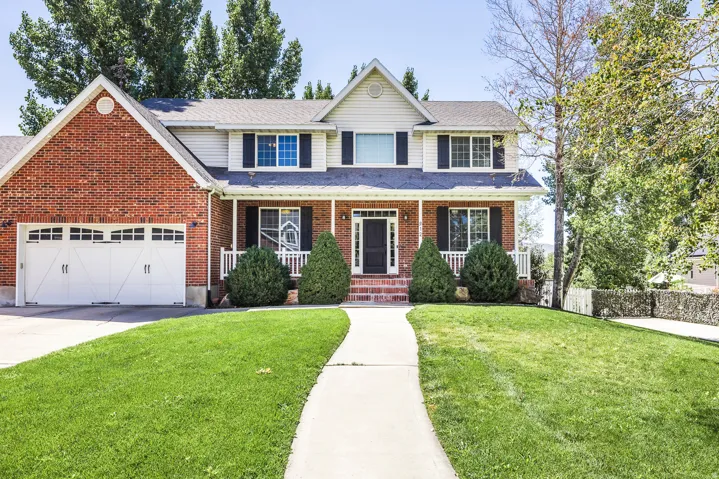 Traditional home with covered porch, roof with shingles, driveway, brick siding, and a garage