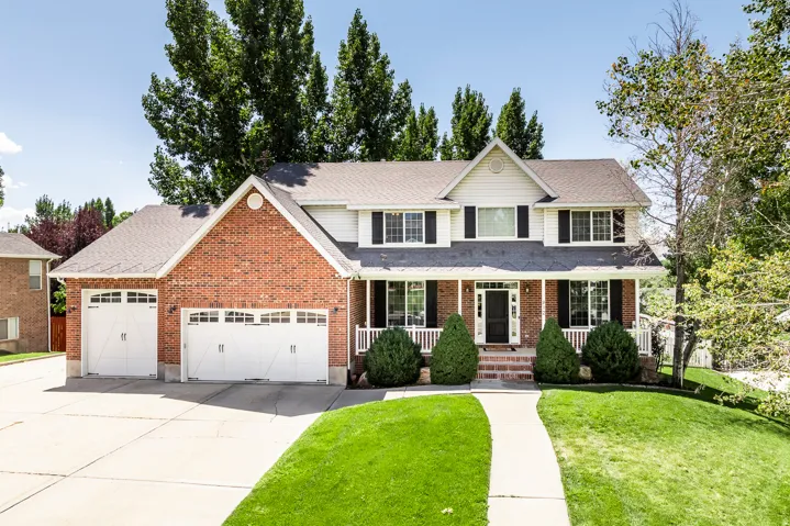 Traditional-style home featuring a front lawn, a garage, covered porch, concrete driveway, and brick siding