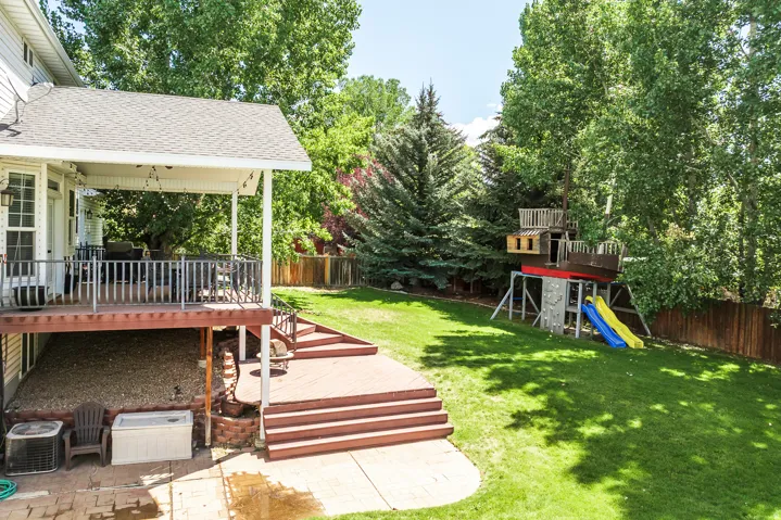 Fenced backyard with a wooden deck, a playground, view of wooded area, and a patio area