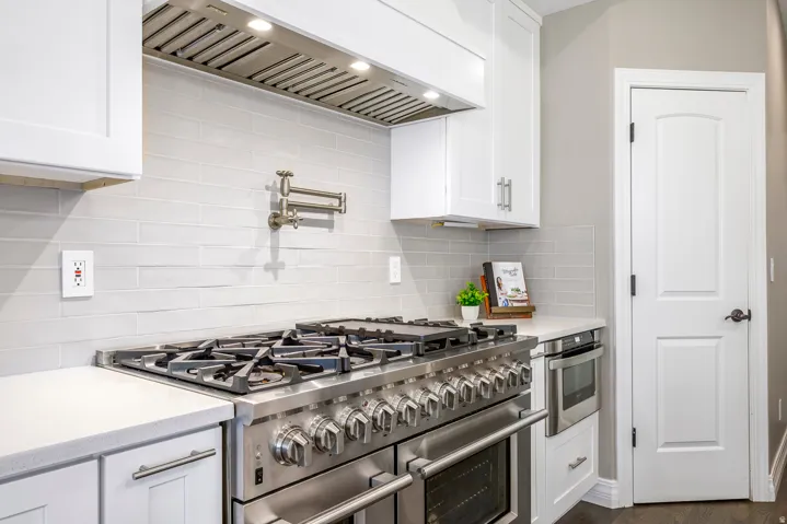 Kitchen featuring double oven range, white cabinets, light stone counters, and backsplash