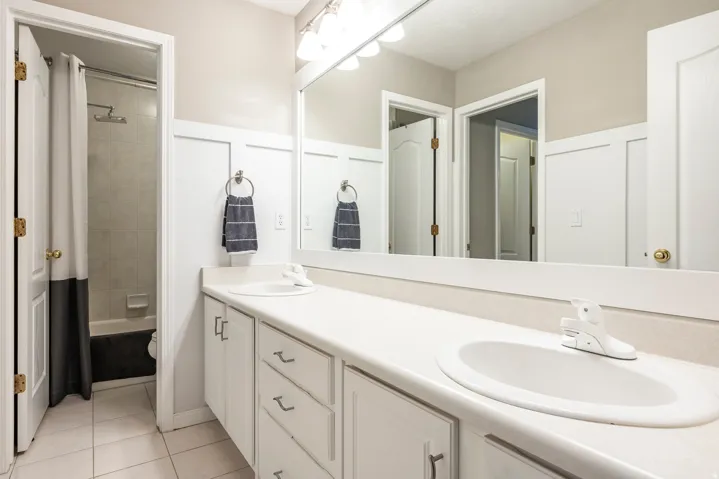 Bathroom featuring double vanity, shower / bathtub combination with curtain, and light tile patterned floors
