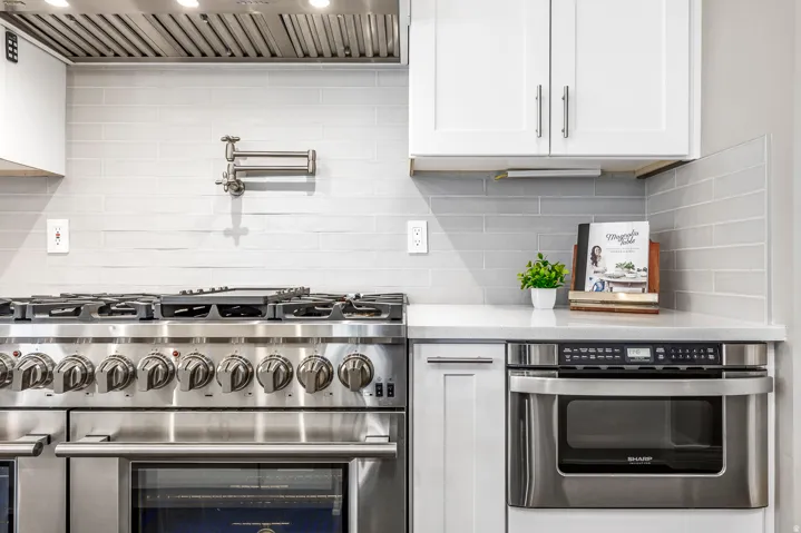 Kitchen with stainless steel appliances, white cabinetry, and light stone counters