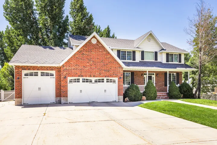 Traditional home featuring an attached garage, driveway, a porch, a shingled roof, and a front yard
