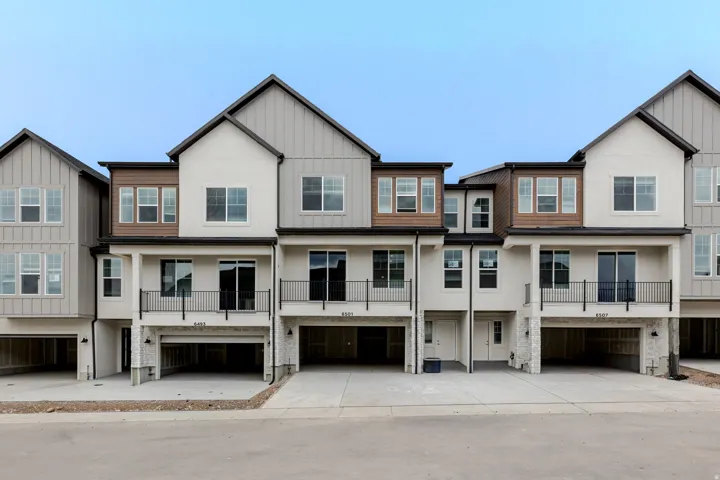 Modern townhome exterior featuring multi-textured siding, private balconies with black railings, and integrated ground-level parking