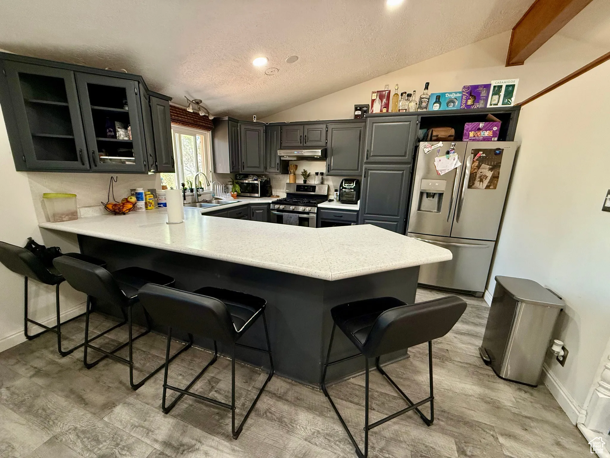 Kitchen with glass fronted cabinets, a breakfast bar, gray cabinets, stainless steel appliances, and a peninsula